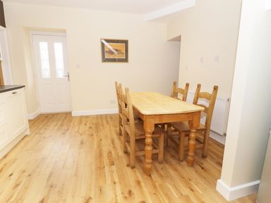 A dining area with a wooden table and four chairs near a white door and kitchen cabinets at The Coach House in Llanrwst