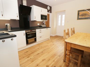 A kitchen with white cabinets black countertops wooden dining table and chairs with a wall clock at The Coach House in Llanrwst