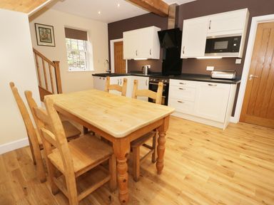 A kitchen with wooden dining table and chairs white cabinets black countertop and wooden floor at The Coach House in Llanrwst
