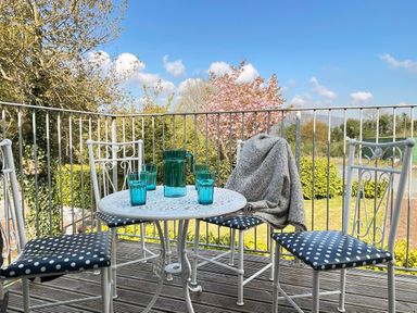 A balcony with a white table and four white chairs with polka dot cushions and a grey blanket on one chair at The Coach House in Llanrwst