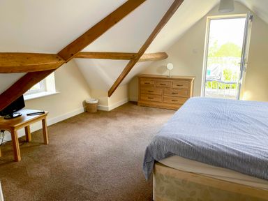 A bedroom with a bed a chest of drawers a small table with a television and a door leading to a balcony at The Coach House in Llanrwst