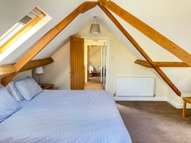A bedroom with wooden beams skylight window bed with blue striped bedding side table with lamp at The Coach House in Llanrwst