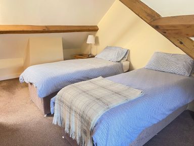 A bedroom with two single beds with bedding and a side table with a lamp at The Coach House in Llanrwst