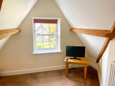 A small room with a window and wooden beams a wooden table with a TV and remote at The Coach House in Llanrwst