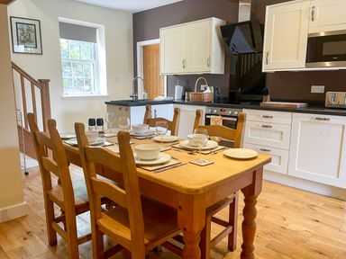 A kitchen with a wooden dining table set for six next to white cabinets and a stove at The Coach House in Llanrwst