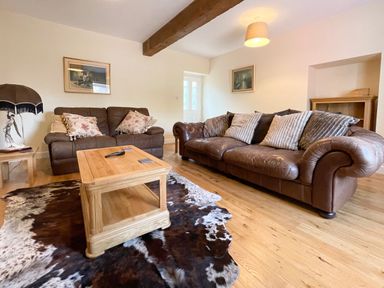 A living room with two brown leather sofas a wooden coffee table a cowhide rug and paintings on the walls at The Coach House in Llanrwst