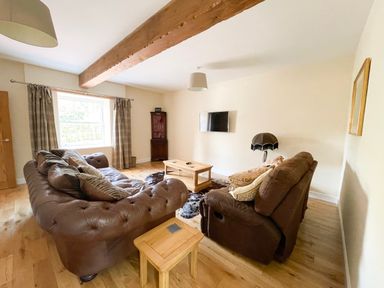 A living room with brown leather sofas a wooden coffee table a cowhide rug a wall-mounted TV and a wooden beam on the ceiling at The Coach House in Llanrwst