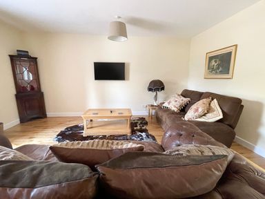 A living room with brown sofas a wooden coffee table a mounted tv and a corner cabinet at The Coach House in Llanrwst