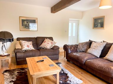 A living room with two brown leather sofas a wooden coffee table a cowhide rug and framed paintings at The Coach House in Llanrwst