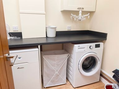 A laundry room with a washing machine a laundry hamper a countertop and a wall cabinet at The Coach House in Llanrwst