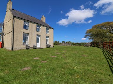 A large two-story house with a green lawn and outdoor chairs next to a wooden fence at Ty Mawr in Llanddaniel Fab