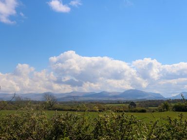 A landscape with green fields bushes and mountains under a blue sky with clouds at Ty Mawr in Llanddaniel Fab