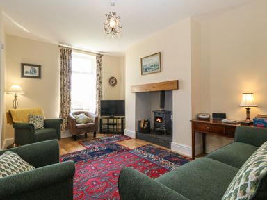 A living room with a wood burning stove a television floral curtains and patterned rugs at Ty Mawr in Llanddaniel Fab