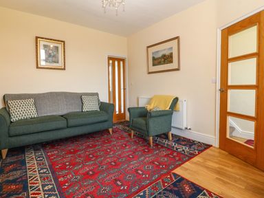 A living room with green sofa and armchair on a large red patterned rug at Ty Mawr in Llanddaniel Fab