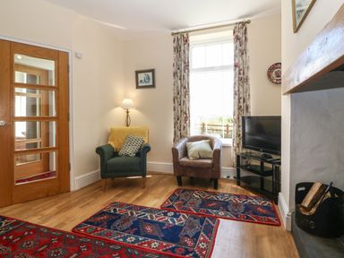 A sitting room with two armchairs a television on a stand and a fireplace with logs at Ty Mawr in Llanddaniel Fab