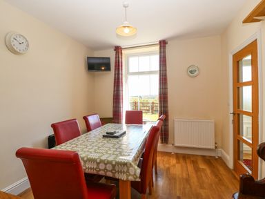 A dining room with red chairs around a table with a patterned tablecloth near a window with plaid curtains at Ty Mawr in Llanddaniel Fab