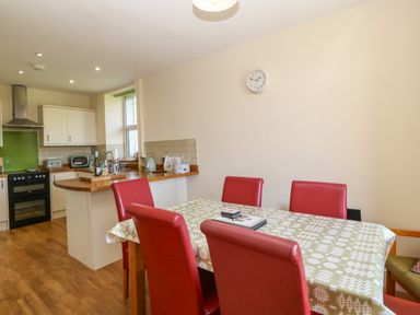 A kitchen and dining area with wooden floor red chairs and a table with a green patterned tablecloth at Ty Mawr in Llanddaniel Fab