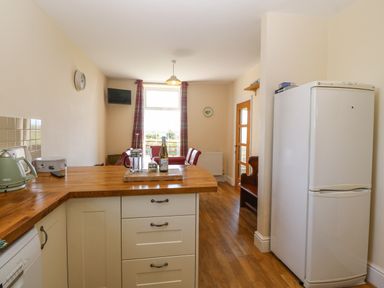 A kitchen with wooden countertops white cabinets a white refrigerator and a dining area with chairs near a window at Ty Mawr in Llanddaniel Fab
