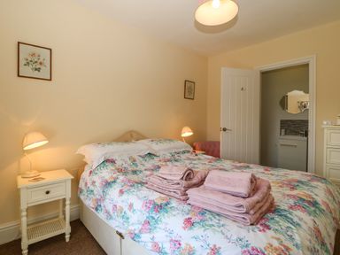 A bedroom with a bed with floral bedspread and towels on top bedside tables with lamps and an open door to a bathroom at Ty Mawr in Llanddaniel Fab