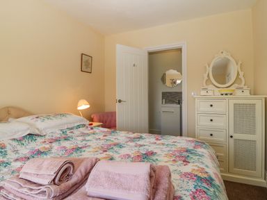 A bedroom with a floral bedspread towels on the bed a dresser with a mirror and an open door leading to a bathroom at Ty Mawr in Llanddaniel Fab