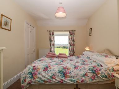 A bedroom with a double bed and floral bedding with folded towels near a window with floral curtains at Ty Mawr in Llanddaniel Fab