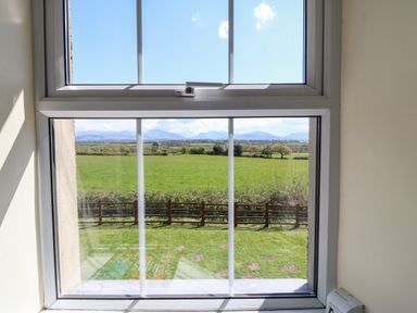 A window looking out to a green field with a wooden fence and hills in the distance at Ty Mawr in Llanddaniel Fab