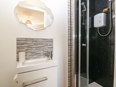 A bathroom with a sink cabinet and wall mirror next to a shower with glass doors at Ty Mawr in Llanddaniel Fab