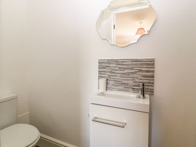 A bathroom with a toilet a small sink with a faucet a wall-mounted mirror and a gray tiled backsplash at Ty Mawr in Llanddaniel Fab