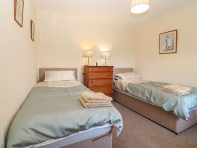 A bedroom with two single beds with folded towels and a wooden chest of drawers with two lamps at Ty Mawr in Llanddaniel Fab