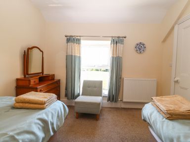 A bedroom with two beds with towels on them a wooden dresser with a mirror a single chair and curtains at Ty Mawr in Llanddaniel Fab