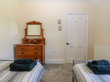 A bedroom with two single beds with towels on them an antique wooden dresser with mirror a white door and light-colored walls at Ty Mawr in Llanddaniel Fab
