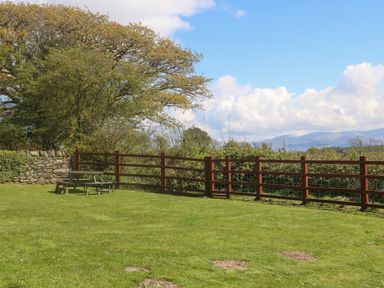 A garden with a wooden picnic bench table a wooden fence trees and mountains in the background at Ty Mawr in Llanddaniel Fab