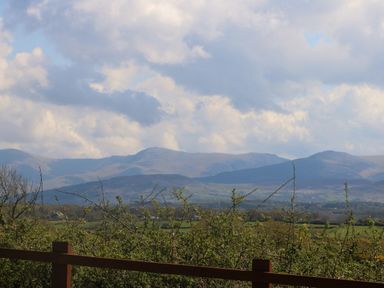 A view of mountains and fields behind shrubs and a wooden fence at Ty Mawr in Llanddaniel Fab