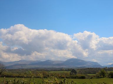 A landscape view of fields trees and mountains under a blue sky with clouds at Ty Mawr in Llanddaniel Fab