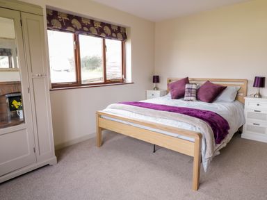 A bedroom with a wooden bed with purple pillows and two white nightstands with purple lamps at The Alders in Llanfyllin