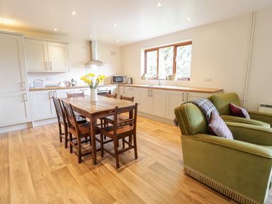A kitchen with wooden table and chairs white cabinets and green armchairs at The Alders in Llanfyllin