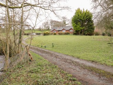 A dirt path leading to a brick house with trees and grass at The Alders in Llanfyllin