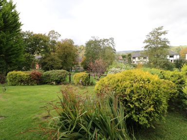 A garden with green grass bushes and trees with houses in the background at The Alders in Llanfyllin
