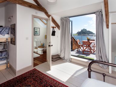 A bedroom with bunk beds and a metal bed frame next to a balcony overlooking water and a castle at Star House in Marazion