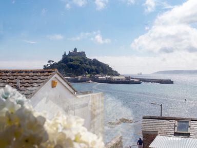 A view of a castle on a hill by the sea with rooftops and a person walking near the water at Star House in Marazion