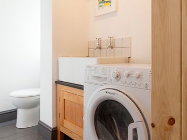 A laundry area with a washing machine beside a utility sink and a toilet in the background at Star House in Marazion