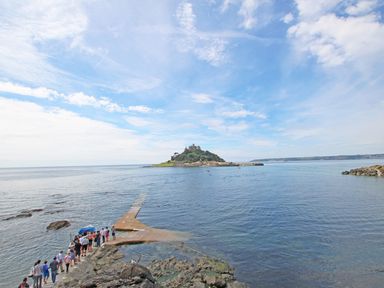 A group of people walking on a pier toward a small island with a castle surrounded by water at Star House in Marazion