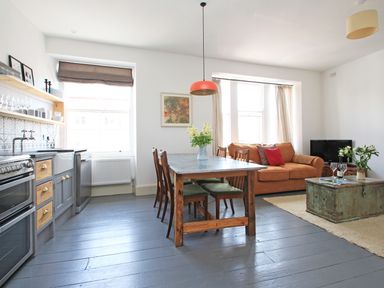 An open plan kitchen and living area with a dining table and chairs an orange sofa and a coffee table at Star House in Marazion