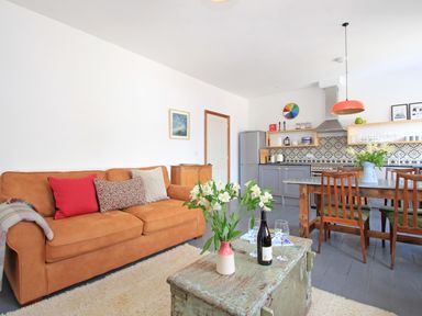A living room with a brown sofa red and patterned cushions a wooden dining table with chairs and flowers in vases at Star House in Marazion