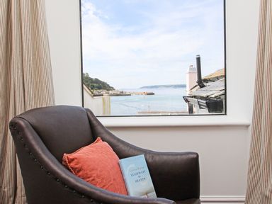 A chair with a cushion and book by a window with a sea view at Star House in Marazion
