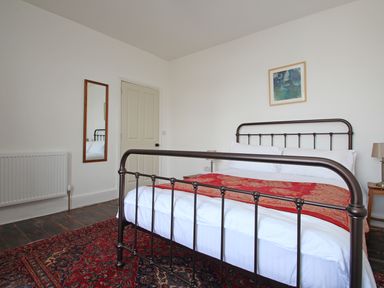 A bedroom with a metal bed frame a red rug a wall mirror and a painting at Star House in Marazion