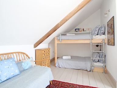 A bedroom with bunk beds a small wooden chest a wooden framed sofa with cushions and a rug at Star House in Marazion