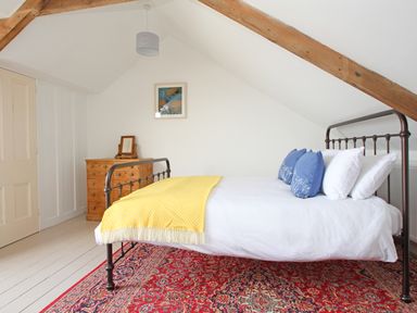 A bedroom with a metal bed frame yellow blanket blue and white pillows wooden chest of drawers and a framed picture on the wall at Star House in Marazion