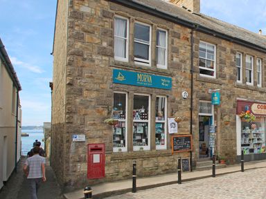 A cobblestone street with a stone building housing Morva gift shop and nearby shops at Star House in Marazion