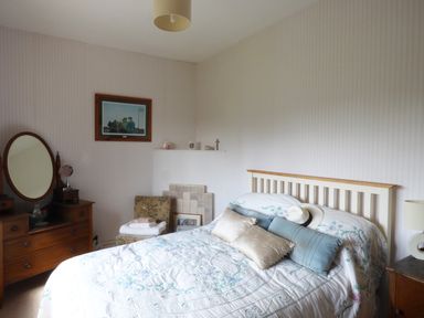 A bedroom with a bed with pillows and hats a wooden dresser with an oval mirror a chair with towels and a framed picture a lamp and a wall painting at Maifield in Carrick-On-Suir County Tipperary